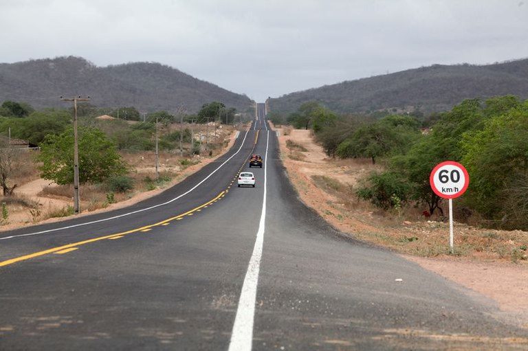 Dois carros trafegam numa rodovia durante o dia